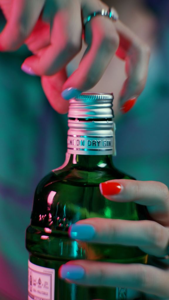 mână femeie cu unghii colorate in timp ce desface o sticlă de gin tanquerai cadru apropriat