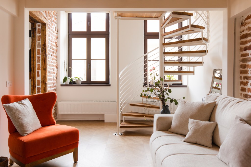 apartament amenajat cu scara in spirala culori neutre si fotoliu portocaliu