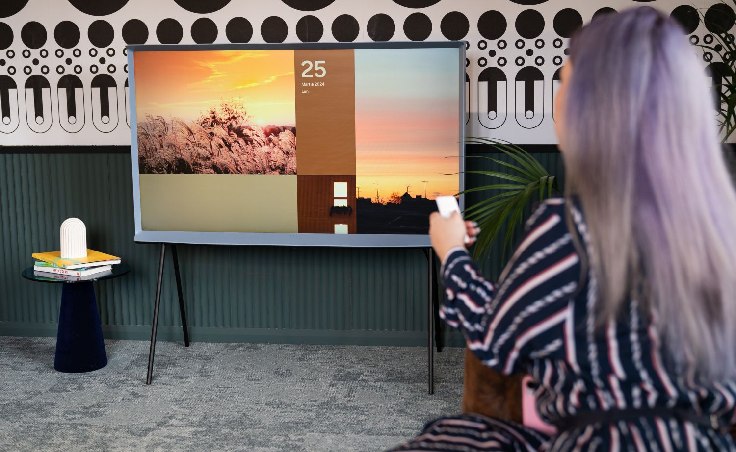 Televizor Samsung The Serif intr-o amenajare de living mic colorata cu tapet pe pereti si femeie care schimba postul