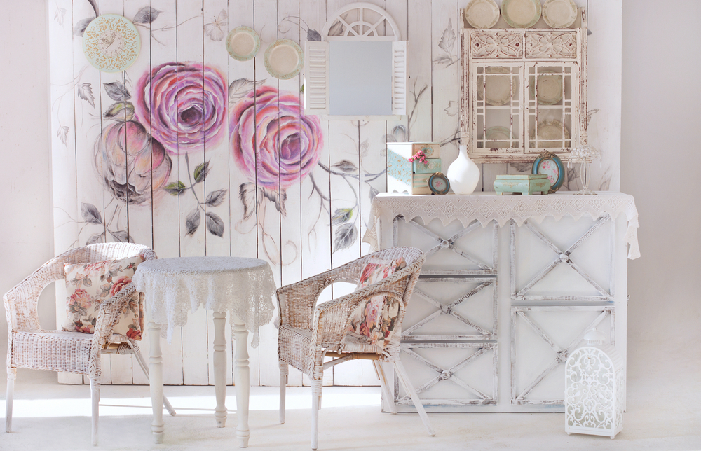 O cameră în stilul shabby chic, cu tapet floral, mobilier din lemn alb cu vopseaua scorojită.