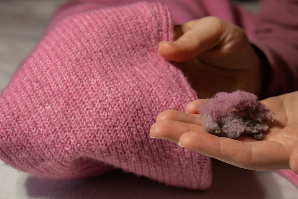 Remedii haine scămoșate: o mână de femeie ține o mulțime de haine, în timp ce cealaltă mână ține un pulover roz curățat de scame.