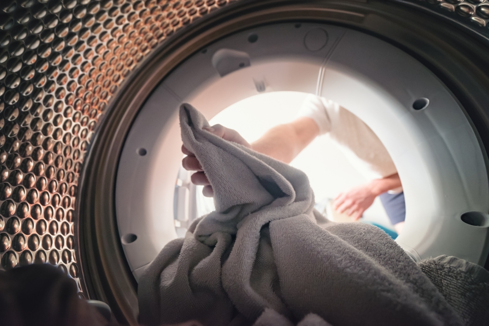 Remediu haine intrate la apă: fotografie din interiorul mașinii de spălat, din care mâinile unei persoae scoate articole textile.