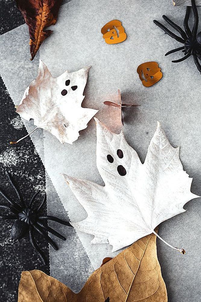 Frunze uscate pictate cu alb sidefat și marker negru ca decorațiuni de Halloween cu aspect de fantome.