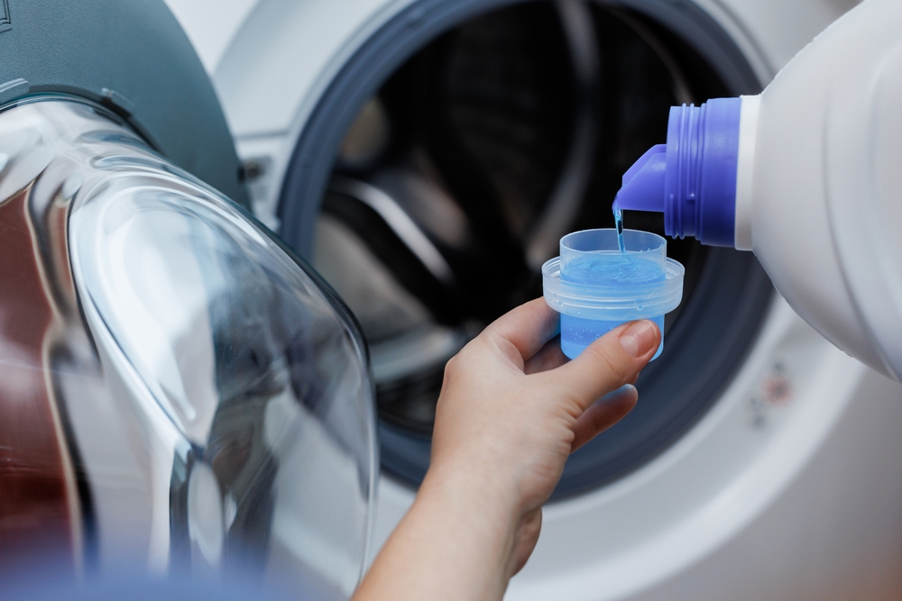femeie toarna detergent lichid in capac inainte de spalarea hainelor