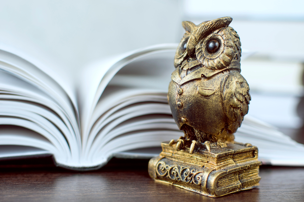 figurina bufnita din metal langa o carte deschisa