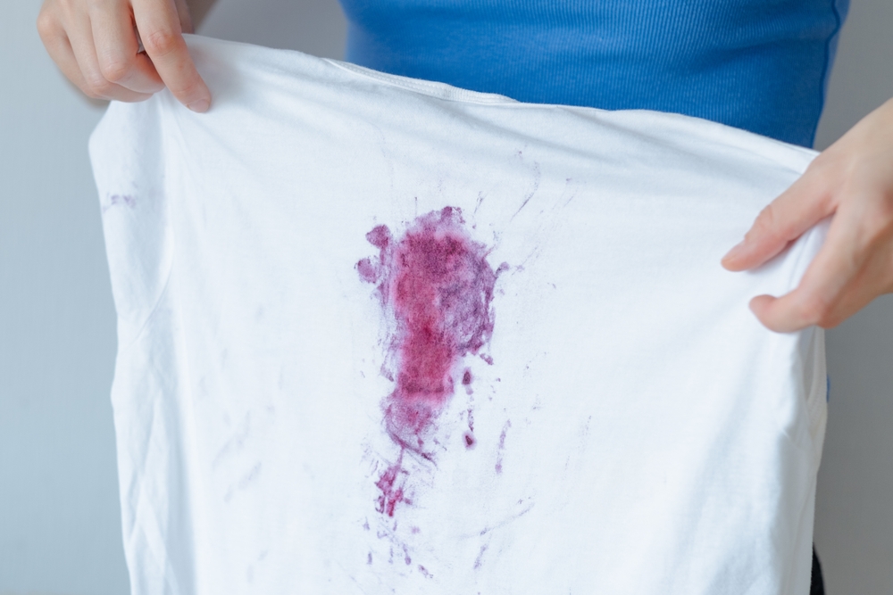 pata struguri pe tricou alb tinut in mana de femeie imbracata in albastru