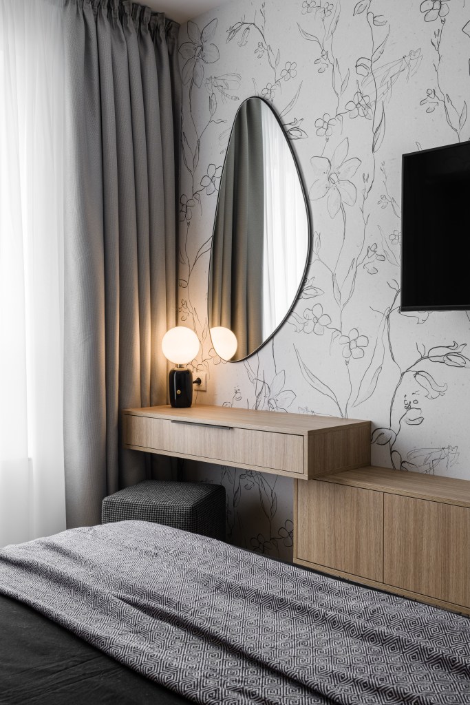 zona cu masuta de machiaj in dormitor perete cu tapet model floral mobilier mdf cu finisaj lemn natur accesorii textile gri