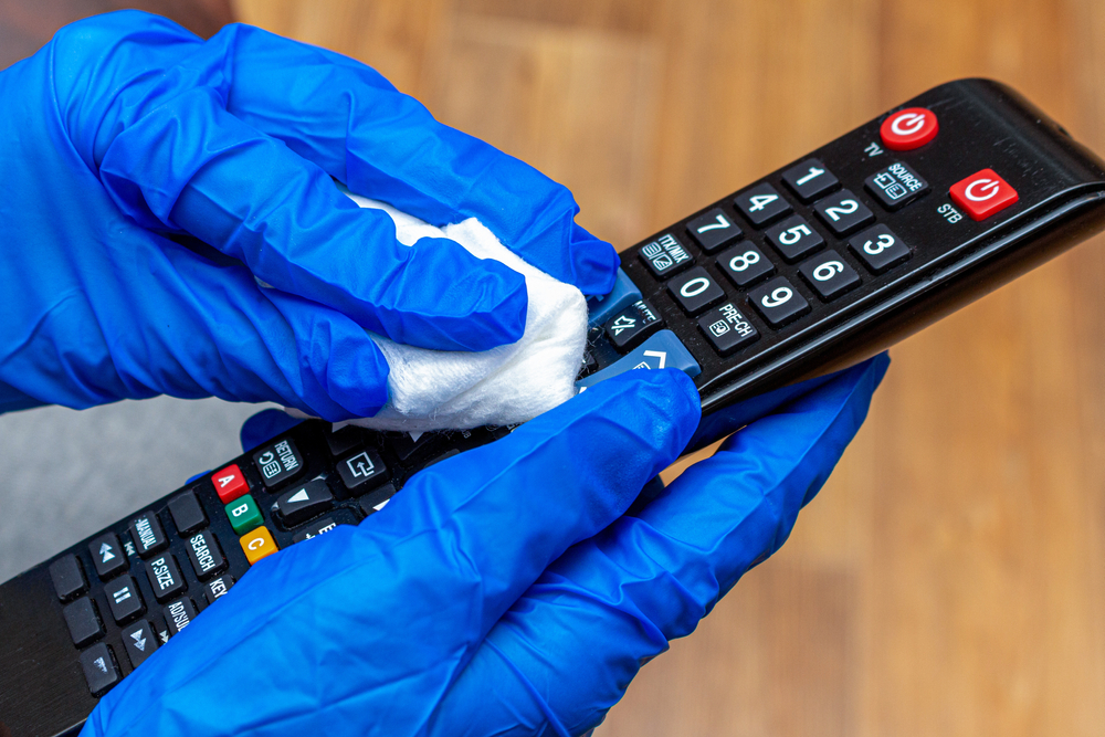curatare igienizare telecomanda tv de catre persoana cu manusi albastre