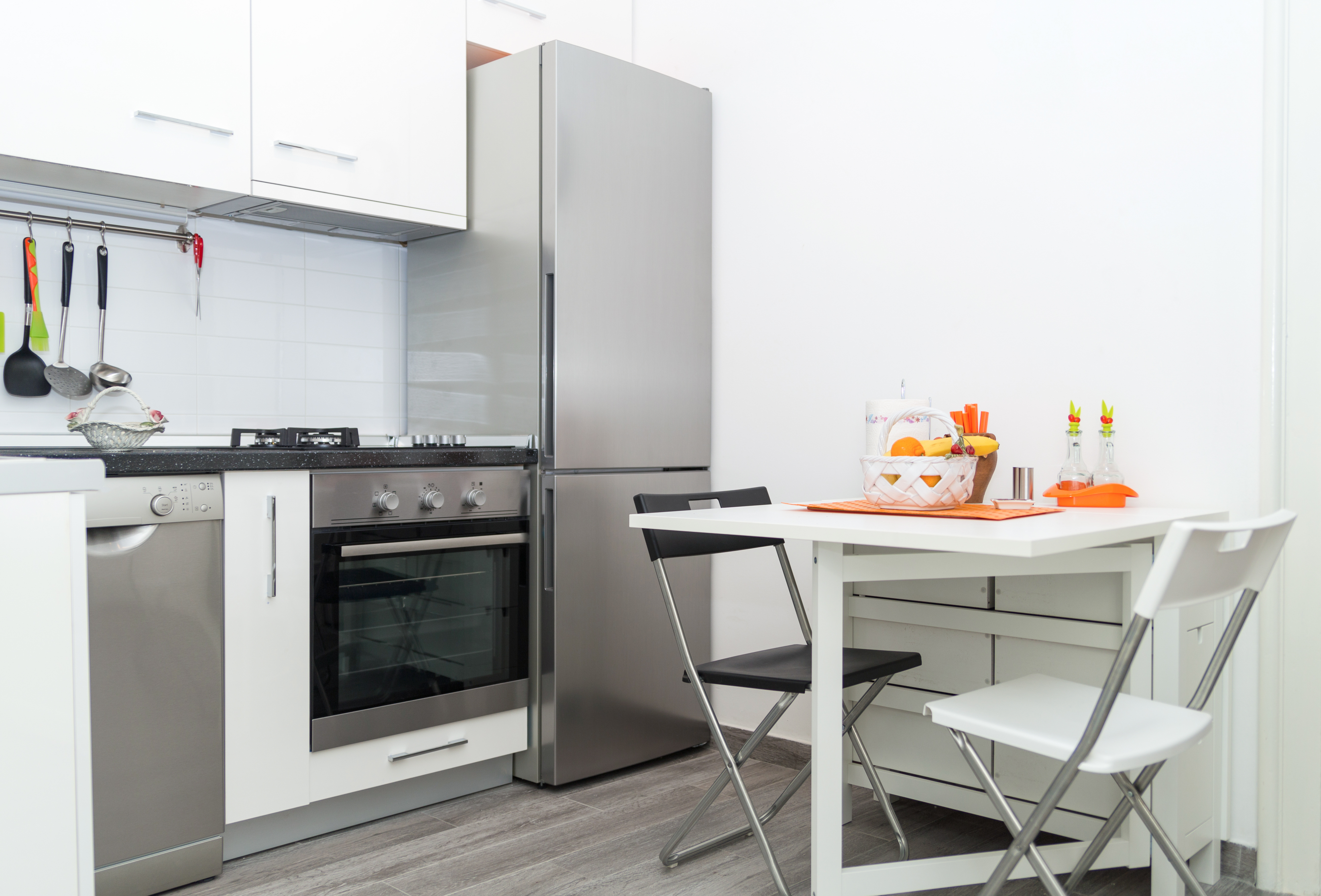 distanta frigider perete intr-o bucatarie cu pereti albi mobilier alb cuptor masa cu scaune