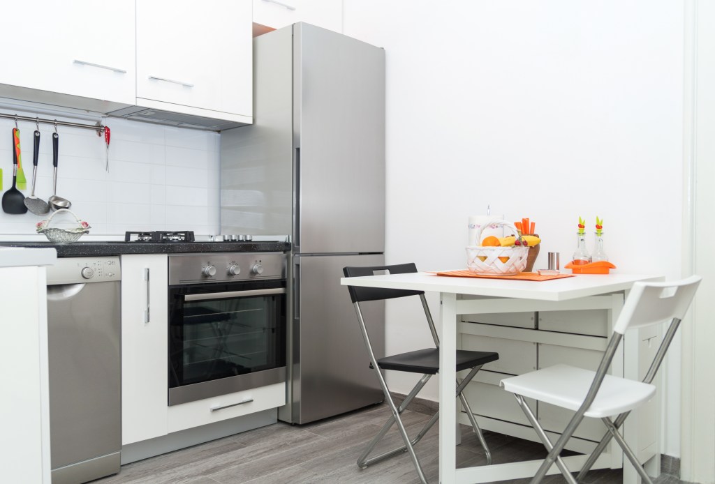 distanta frigider perete intr-o bucatarie cu pereti albi mobilier alb cuptor masa cu scaune