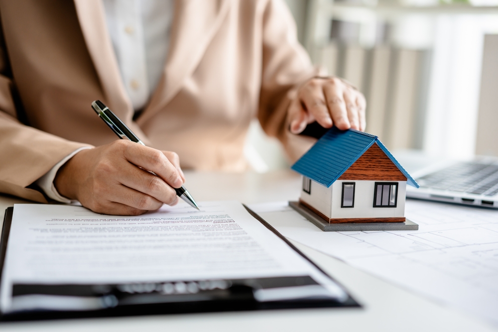cost acte casa femeie semnează actele casei cu mana pe o casa în miniatura