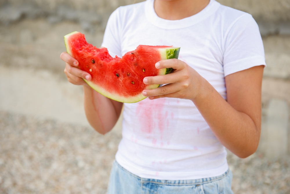 copil cu felie de pepene rosu si pete pe tricou alb