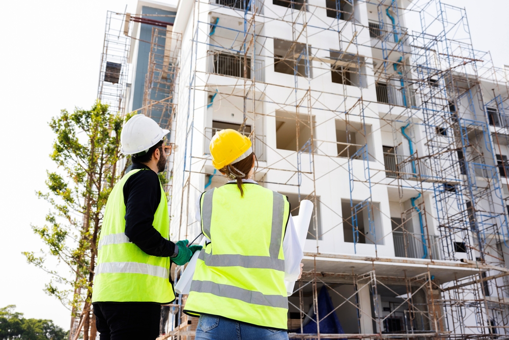 ingineri constructori cu veste verzi in fata unui bloc de apartamente in construcție