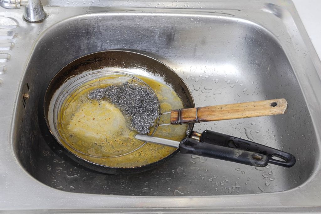 de ce nu se arunca uleiul in chiuveta imagine cu o tigaie plina cu ulei alimentar uzat asezata intr-o chiuveta de bucatarie