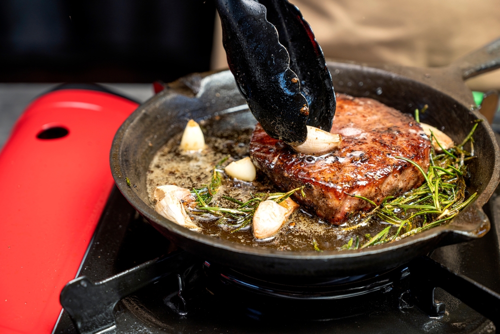 friptura preparata intr-o tigaie de fonta cu rozmarin si usturoi pe aragaz