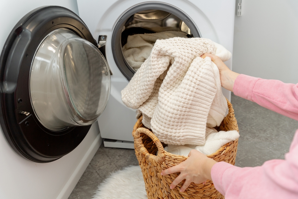 haine din lână spălate la mașina de spălat de către femeie care le pune in cuva
