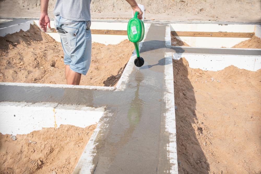 fundație casa din beton udare cu apa de către muncitor cu stropitoare