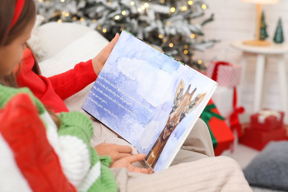 fetita citeste o carte pentru copii pe canapea langa brad cadouri de craciun