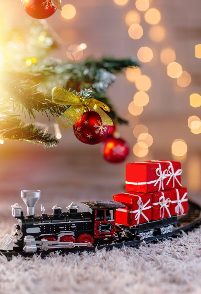 cadou de craciun pentru copii trenulet de jucarie asezat sub un brad cu globuri si luminite