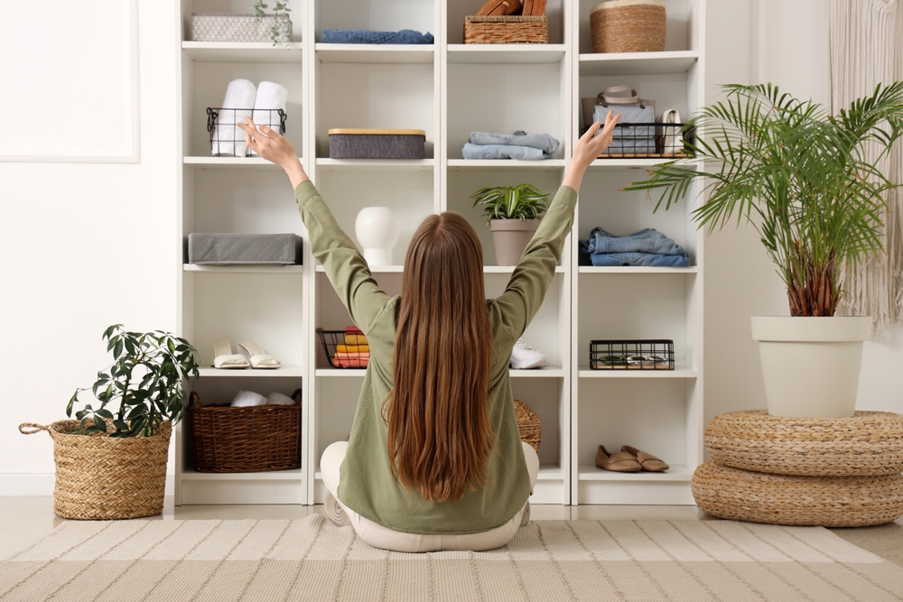Curățenie generală cu metoda Oosouji: O femeie șatenă cu părul lung stă în fața dulapului de haine frumos organizat și ridică brațele în sus de bucurie în timp ce stă pe covor turcește.
