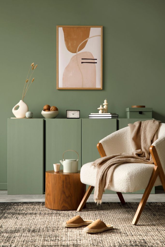 tendinte culori 2026 perete vopsit verde eucalipt cald cu fotoliu alb si covor bej-crem cu taburet teracotta si tablou in nuante de caramiziu si roz
