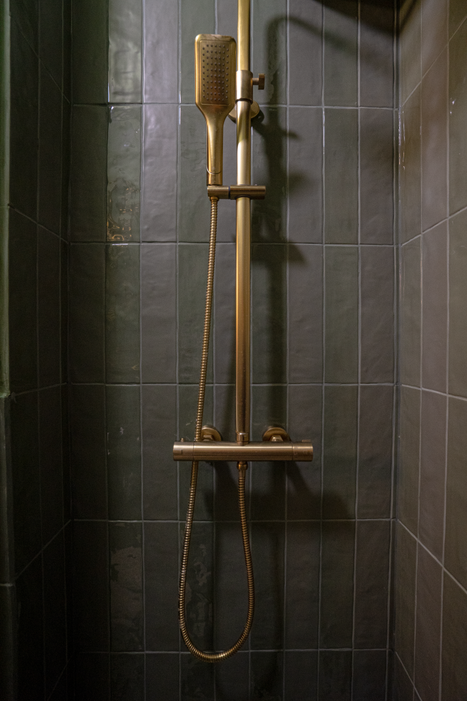 zonă de duș placată cu faianță dreptunghiulară verde pădure, aplicată vertical, cu obiecte sanitare aurii