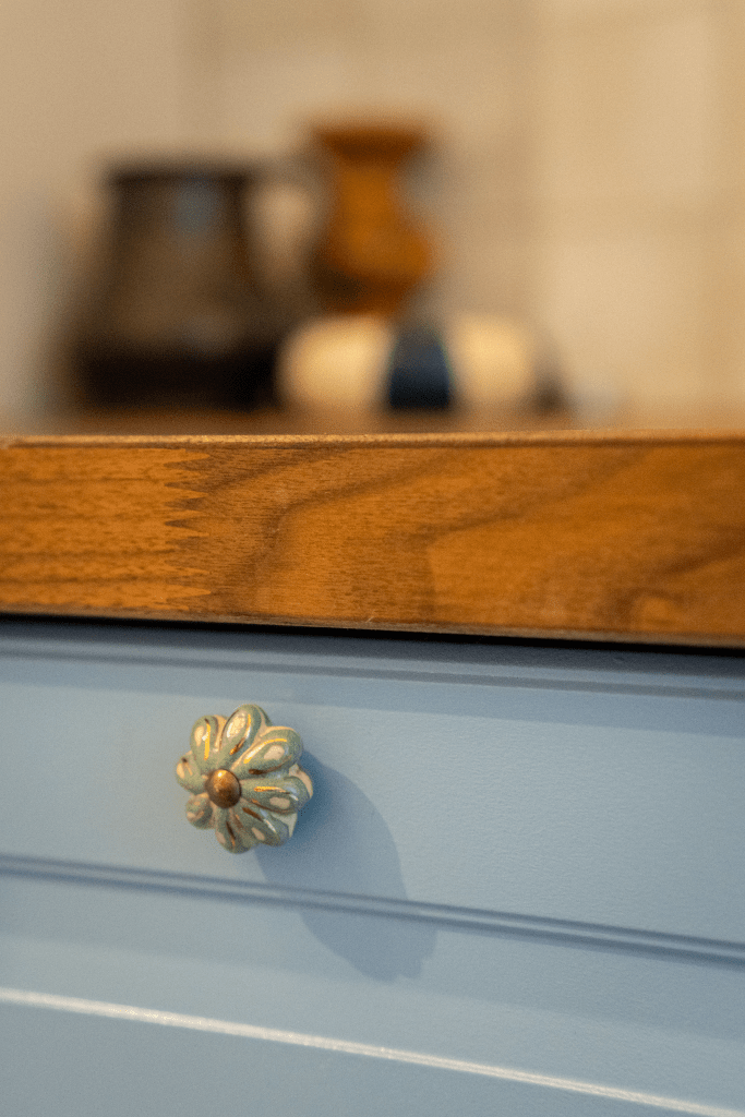detaliu mobilier de bucatarie bleu pastel cu blat din lemn si maner pentru dulap in forma de floare cu aspect vintage
