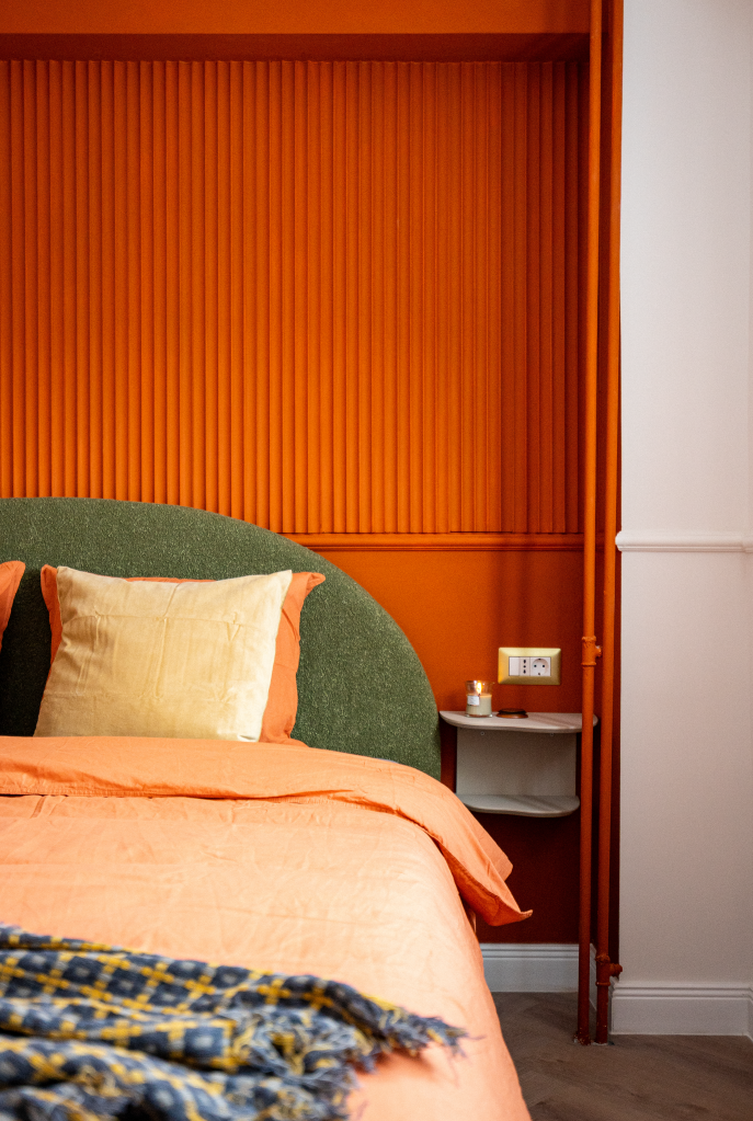 dormitor cu perete oranj portocaliu intens tevi vopsite in portocaliu pat cu tablie tapitata verde padure si asternuturi portocalii