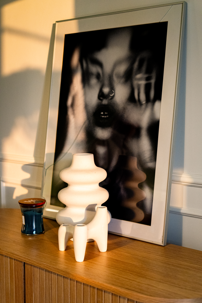 layout cu tablou alb negru, vaza sculpturala si mici decoratiuni asezate pe o comoda din lemn natur