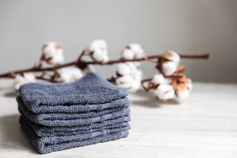 La cât timp se spală prosoapele de față: Prosoape de față bleumarin pudrat pe o puprafață albă, alături de o creangă cu flori de bumbac.
