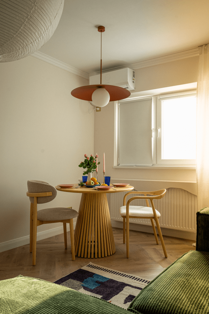 amenajare living cu pereti albi canapea verde perne decorative portocalii covor alb cu roz si nleumarin si masa cu scaune din lemn natur si tapiterie din boucle alb