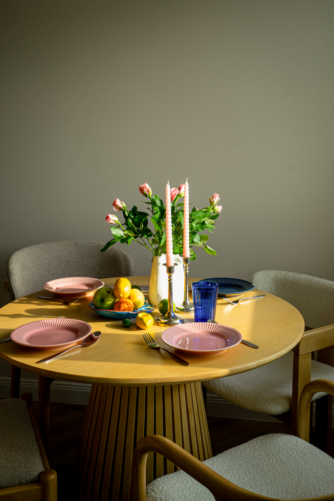 masa de dining din lemn cu scaune tapitate cu boucle alb farfurii din ceramica roz si bleumarin si o vaza cu trandafiri