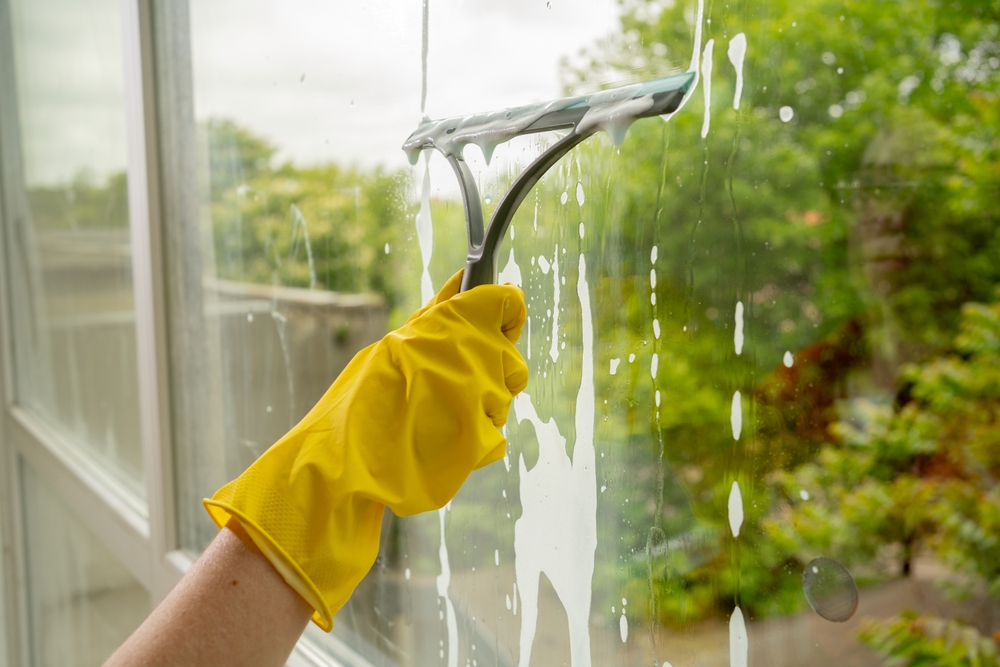 geamuri spălate și curățate cu bicarbonat de sodiu de către femeie cu mănuși galbene si racleta