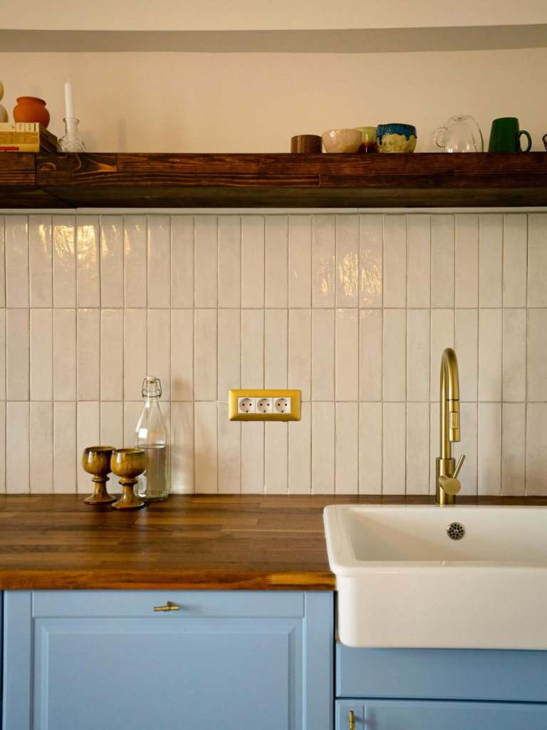 bucatarie amenajata cu faianta verticala alba obiecte sanitare aurii blat din lemn si lavoar alb montate pe un mobilier cu fronturi bleu pastel