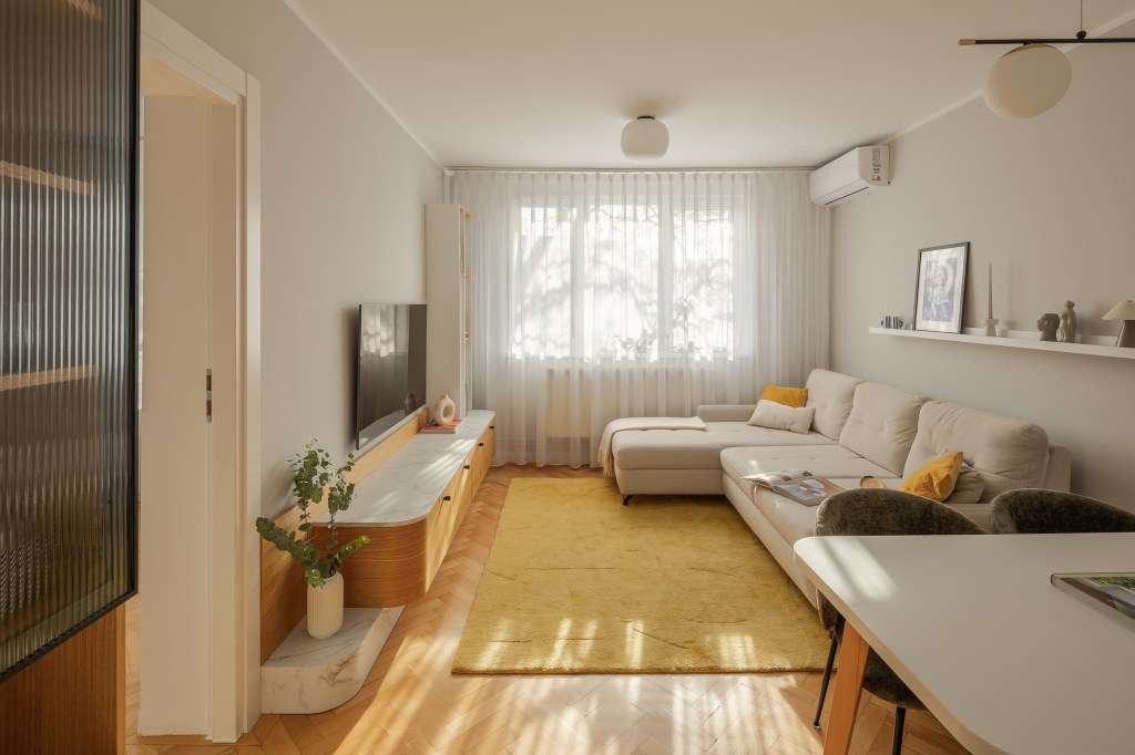 amenajare living stil scandinav cu influente mid century modern si japandi, cu parchet din lemn masiv in format herringbone si coltar alb pereti gri deschis si comoda din lemn in nuanta calda