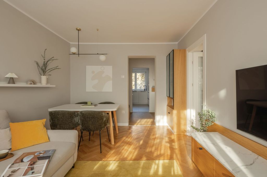 amenajare living stil scandinav cu influente mid century modern si japandi, cu parchet din lemn masiv in format herringbone si coltar alb pereti gri deschis si comoda din lemn in nuanta calda