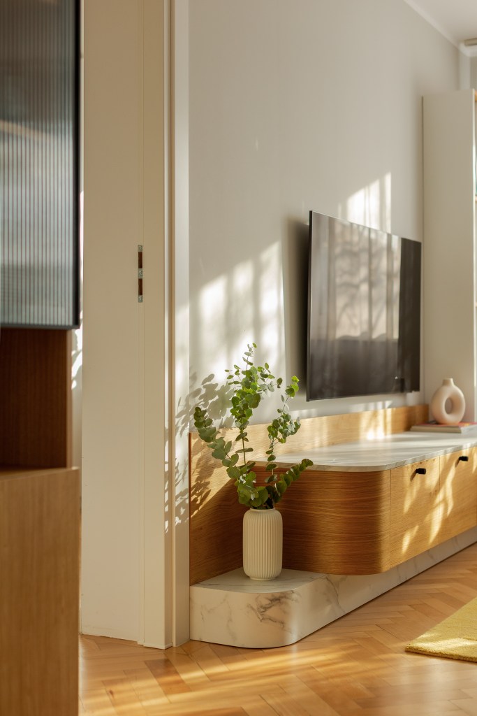 amenajare living stil scandinav cu influente mid century modern si japandi, cu parchet din lemn masiv in format herringbone si coltar alb pereti gri deschis si comoda din lemn in nuanta calda