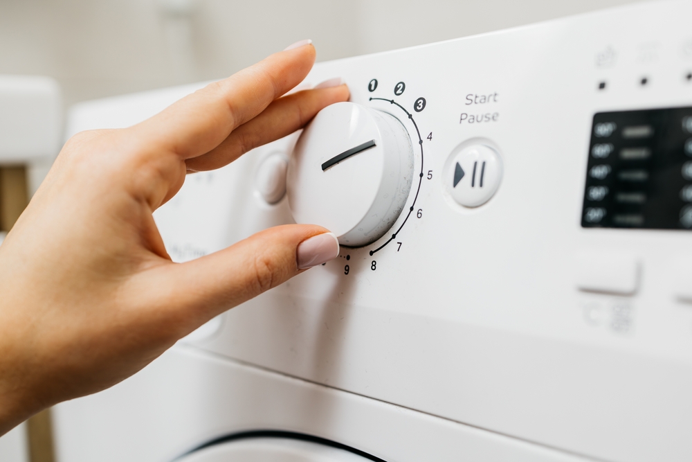 Mână de femeie potrivește programul la mașina de spălat haine.