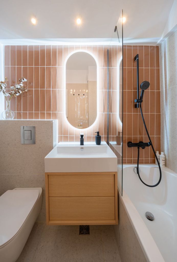 amenajare baie cu ceramica portocalie oglinda ovala cu lumini led masca de chiuveta lemn natur si cada