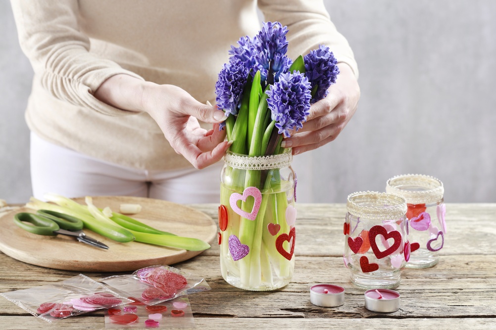 La ce temperatură se țin zambilele: O femeie aranjează un buchet de zambile albastre într-o vază transparentă cu modele roșii.