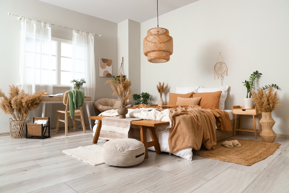 dormitor amenajat în stil boho cu lustră din ratan mobilier din lemn natur vaze cu stuf și covoraș din iută