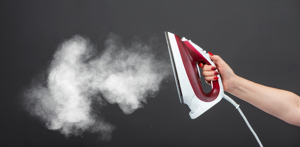 fier de călcat încins aburi ținut in mana de femeie 