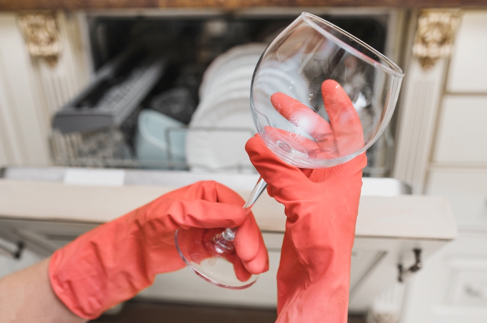 pahar spălat cu pete de calcar ținut in mana de femeie cu mănuși