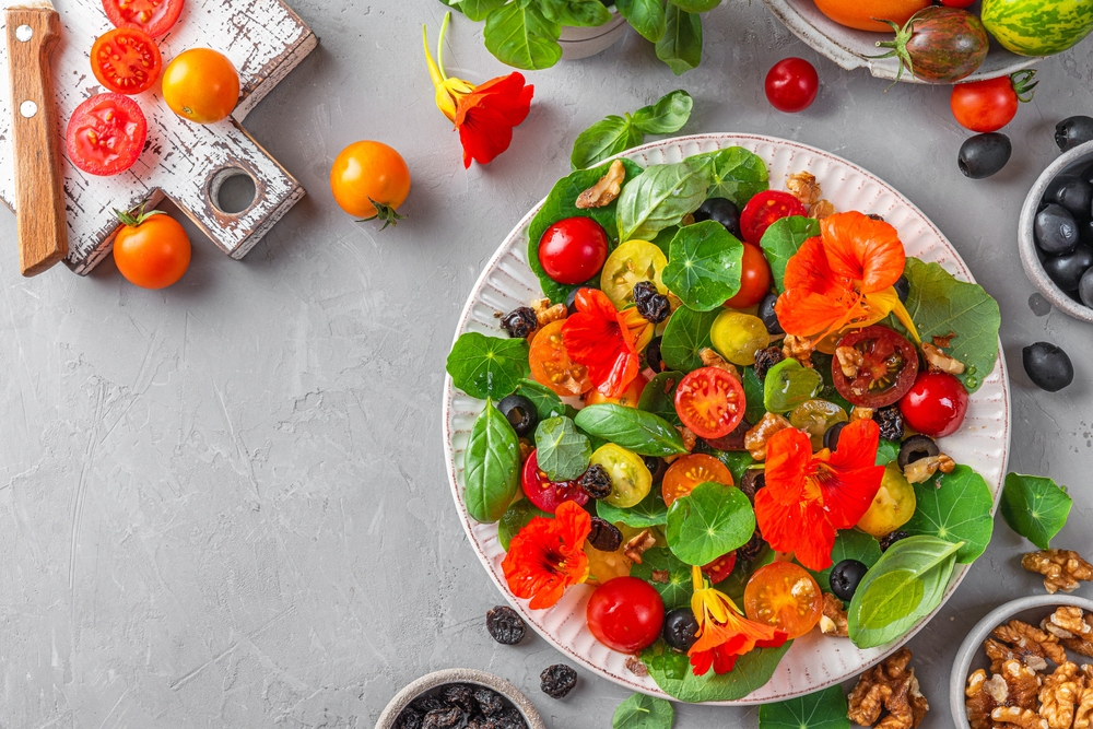 O salată de legume cu flori de năasturel într-un bol alb pe p masă albă.