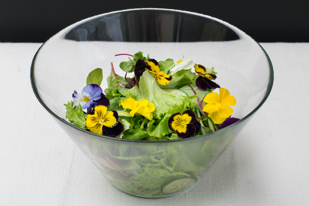 Flori comestibile: Un bol transparent din sticlă cu salată decorată cu panseluțe. 